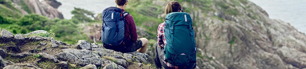 Two hikers wearing Thule backpacks sitting on rocks, enjoying the view.